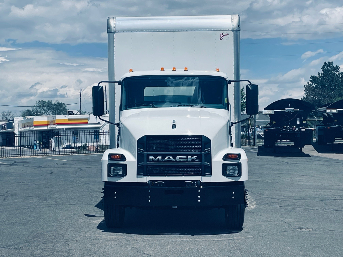 Front view of a white 2026 Mack MD6 box truck showing front grille with Mack logo and headlights, cargo box in background.