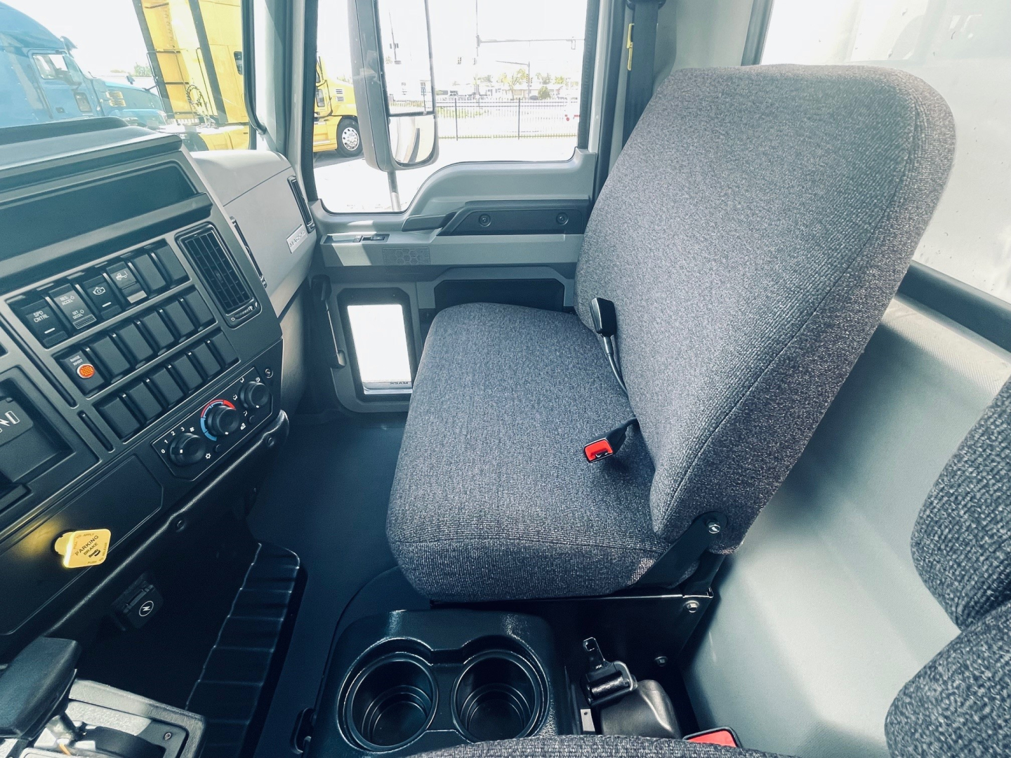 Cab interior of a Mack MD6 truck showing steering wheel, dashboard with controls, driver seat and cup holders.