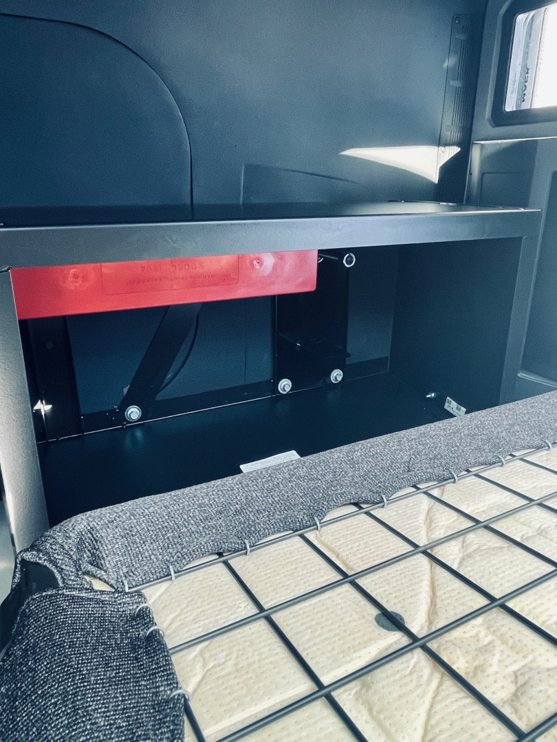 Mack MD6 truck cargo area showing empty storage cavity with red label and metal brackets.