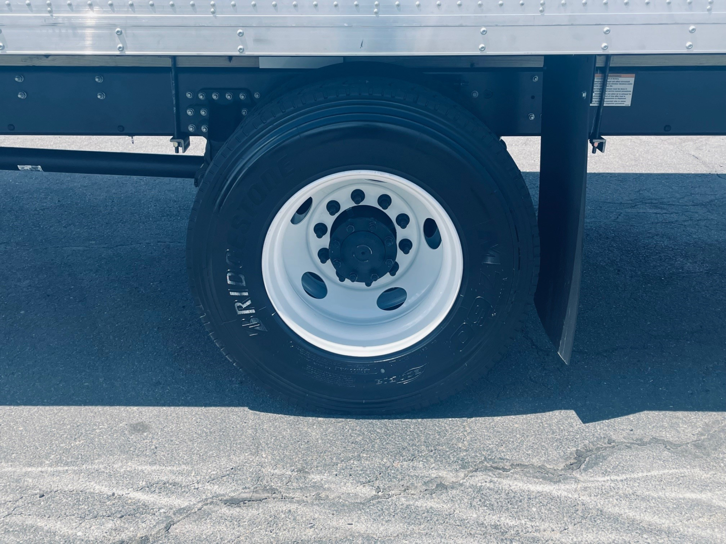 Truck wheel and part of the chassis showing a white steel wheel and black tire under a trailer side, with a spare boot and frame details visible.