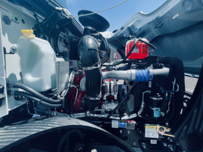 Mack MD6 engine bay showing coolant reservoir, turbocharger piping, alternator, and various hoses and components.
