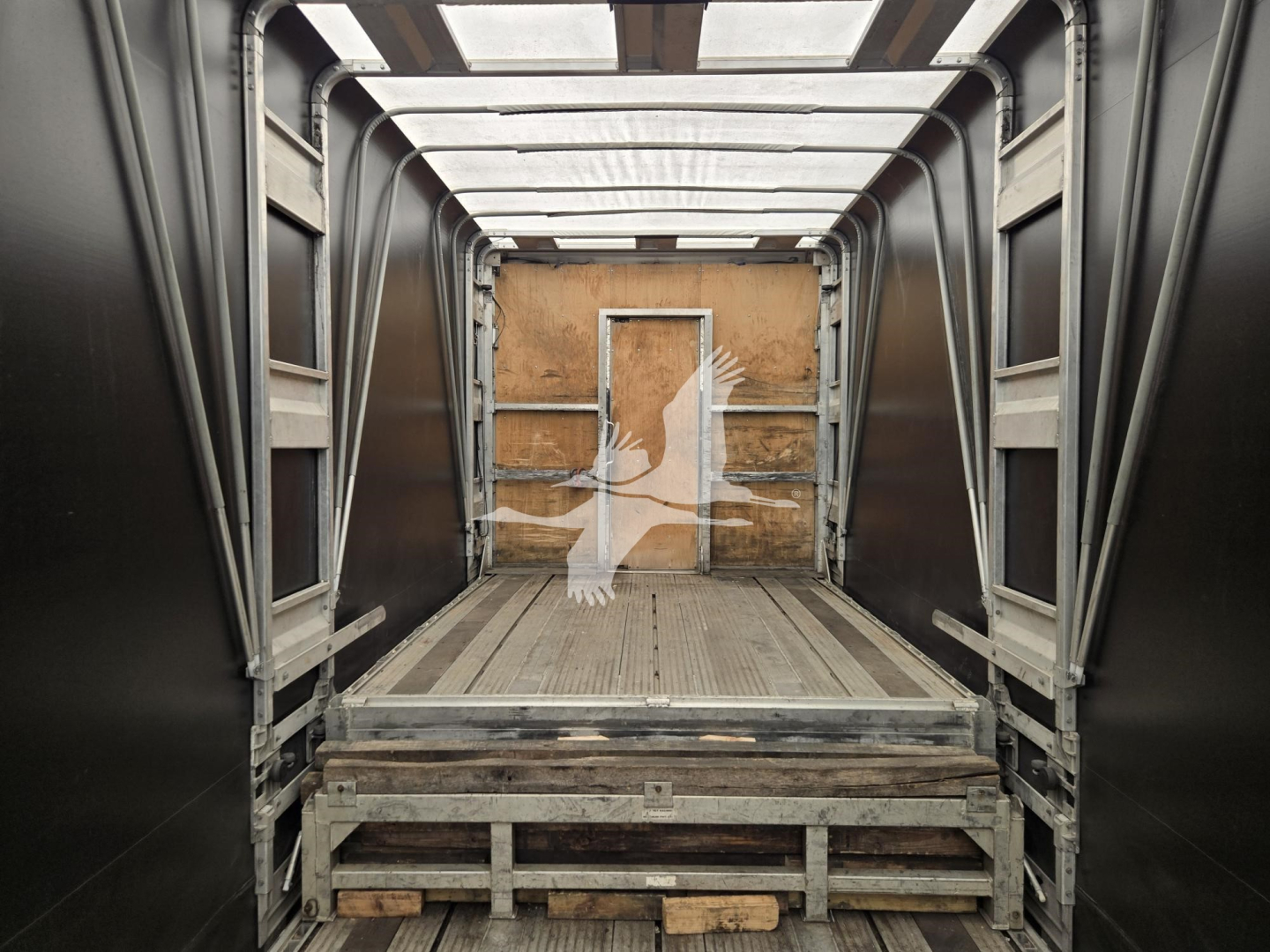 Interior of a 2019 Mac Drop Deck trailer showing loading area with wooden back wall and metal framing; rear door opening visible.
