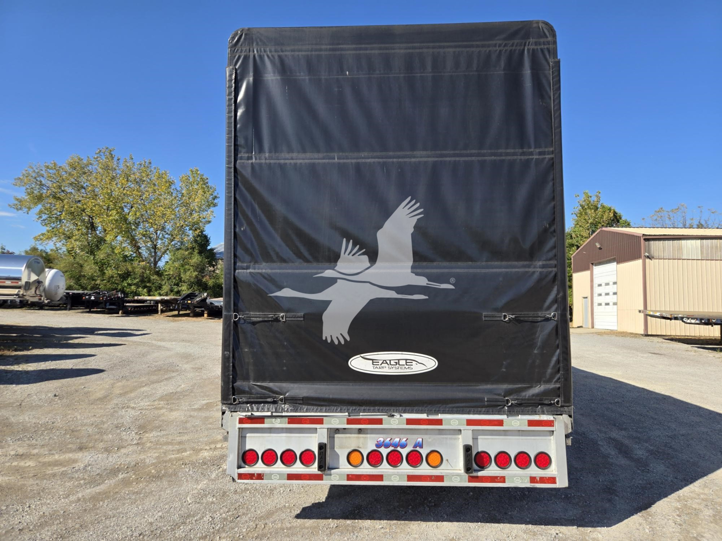 Trailer rear view with black fabric tarp, eagle logo, and taillight assembly of a 2019 Mac drop deck trailer showing back doors and bumper. Serial/stock not legible.