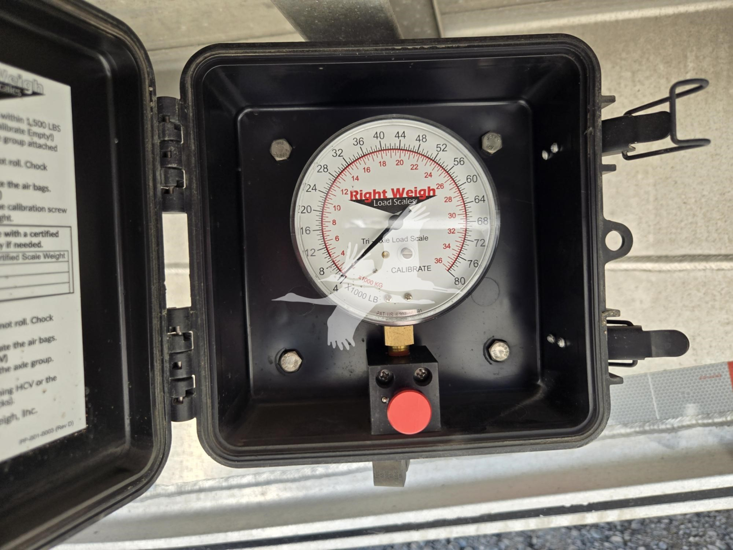 Envelope-style dial gauge in a black protective case mounted on a trailer hitch with a red button and small label, showing a circular Right Weigh scale inside the lid.