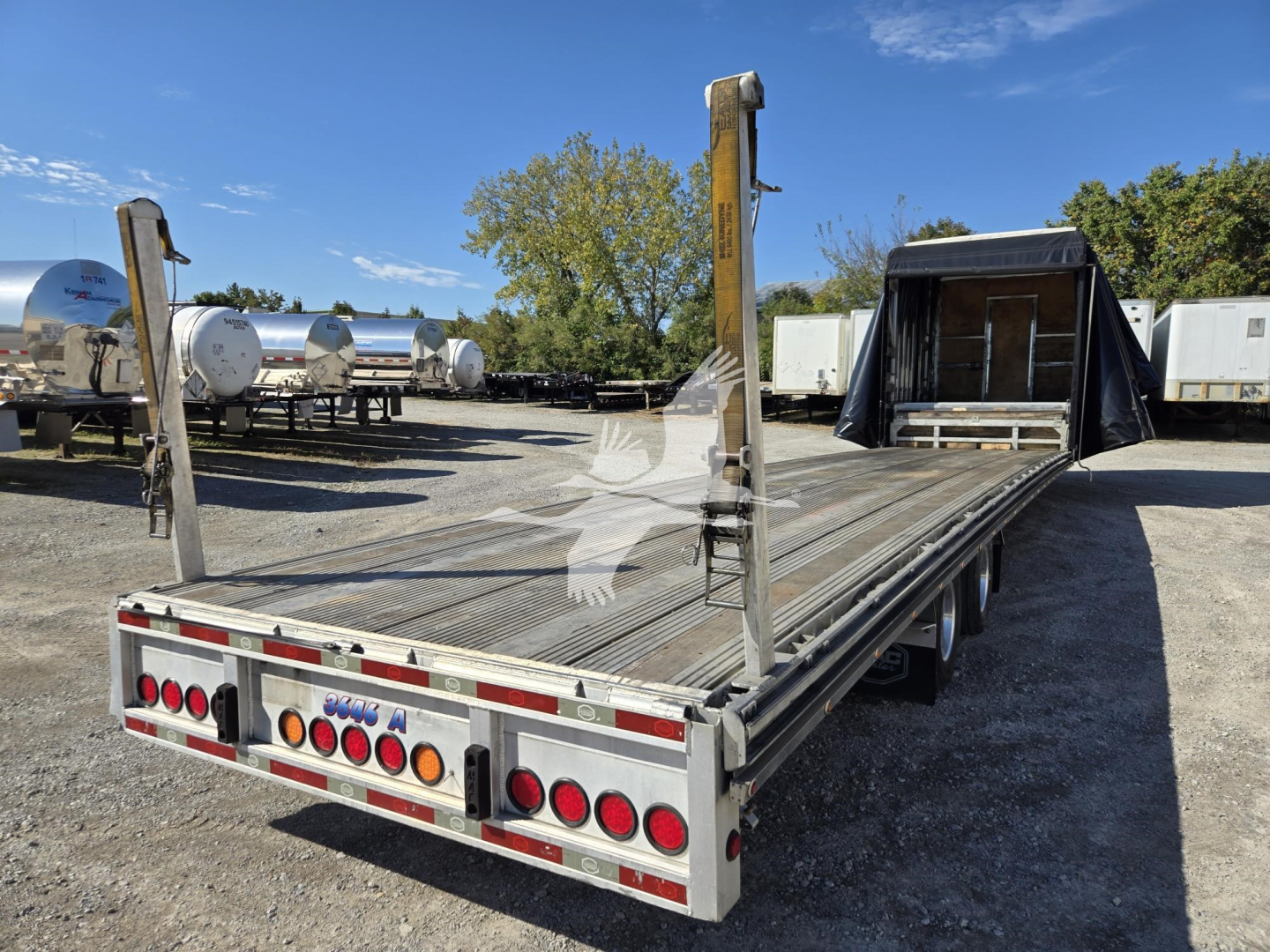 Trailer deck showing metal drop deck with vertical stake posts and rear bumper lights, open loading area, clear sky.