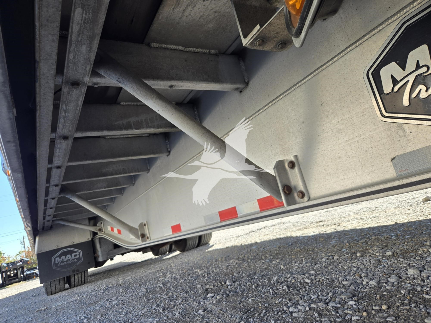 Mac drop deck trailer side view showing MAC logo, hydraulic supports, and reflective stripes.