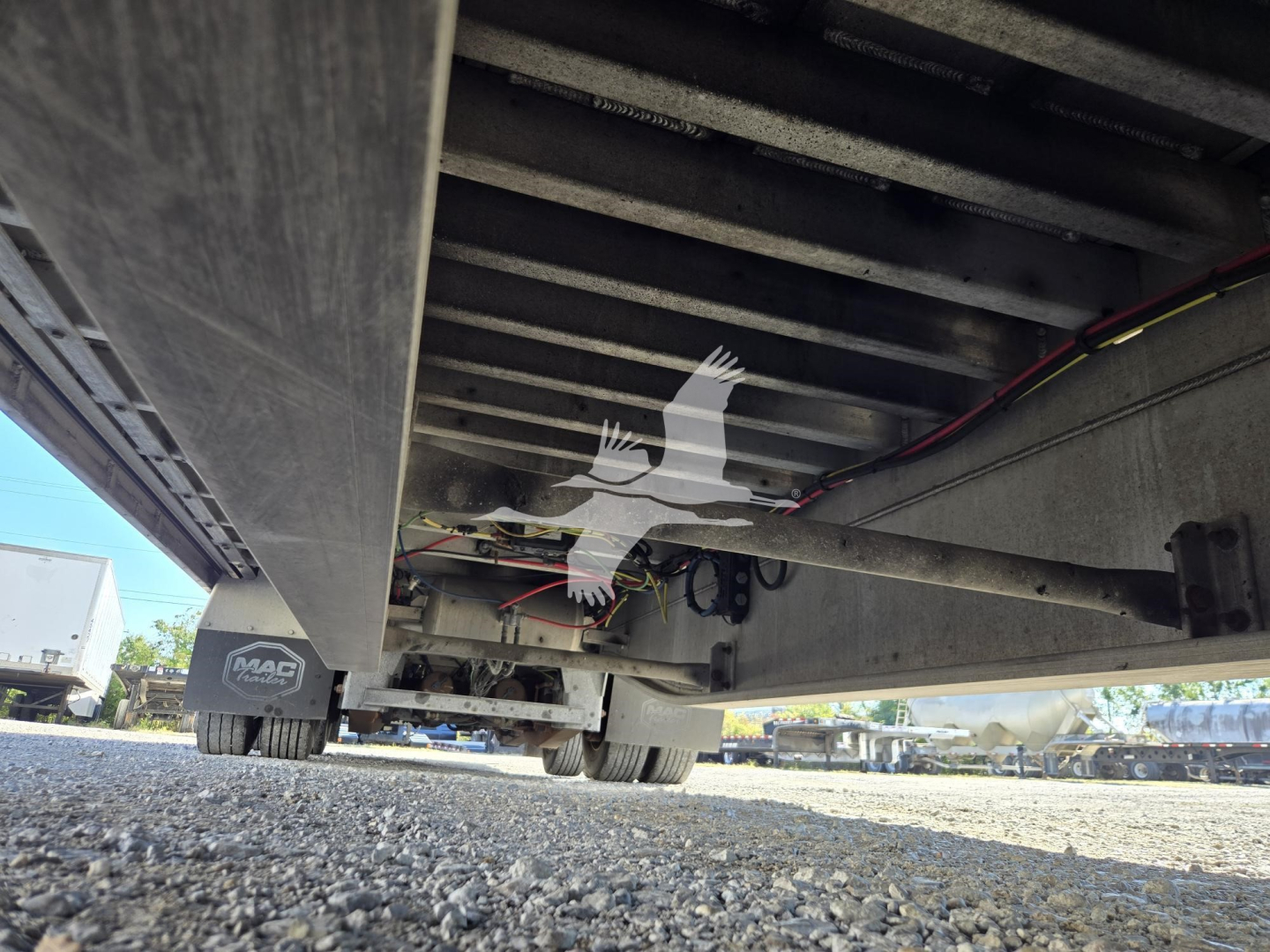 Mac drop deck trailer undercarriage view showing frame rails, suspension, and wiring harnesses in service condition.