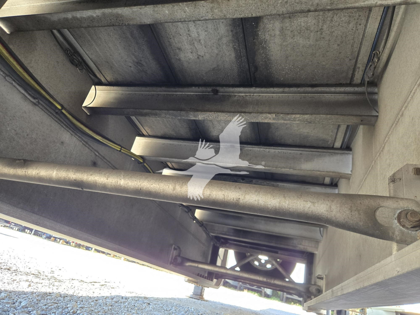 Trailer underside showing structural I-beams, hydraulic line, and support beams on a 2019 Mac Drop Deck trailer.