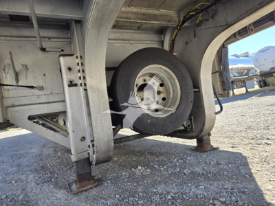 Trailer underside showing spare tire mounted on the frame and landing gear leg in a drop deck trailer.