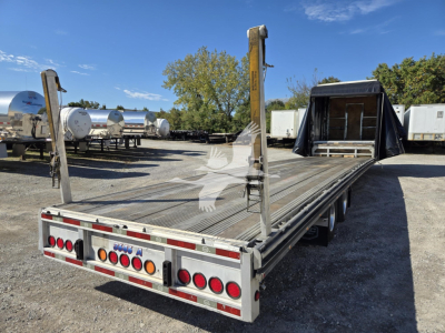 Trailer deck showing metal drop deck with vertical stake posts and rear bumper lights, open loading area, clear sky.