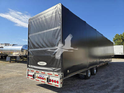 Trailer rear/side view of a 2019 Mac drop deck trailer with a black tarp and a large white flying eagle logo on the side.