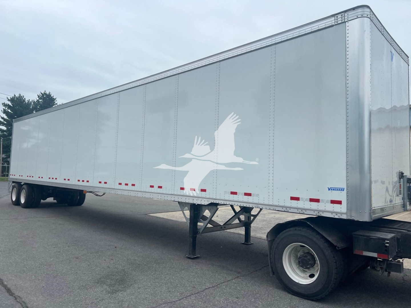 Trailer side with white graphics of two birds in flight and a Vanguard logo, aluminum exterior, rear wheel and hitch area visible.