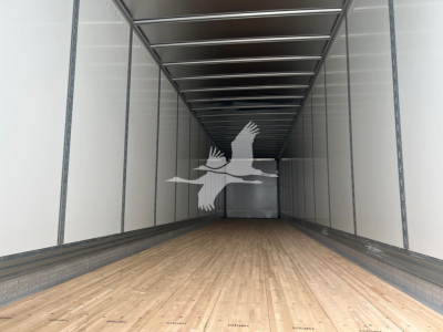 Trailer interior showing wooden floor and metal sidewalls; a white logo of a bird in flight overlays the center of the image.