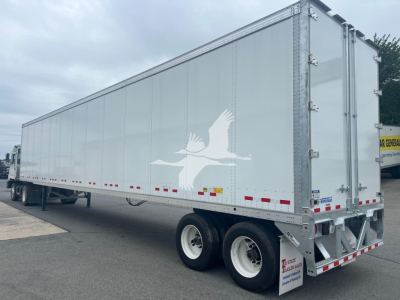 Trailer side view showing a white eagle graphic and reflective red/white safety tape on the lower edge; rear of a Vanguard VXP trailer with dual rear wheels.