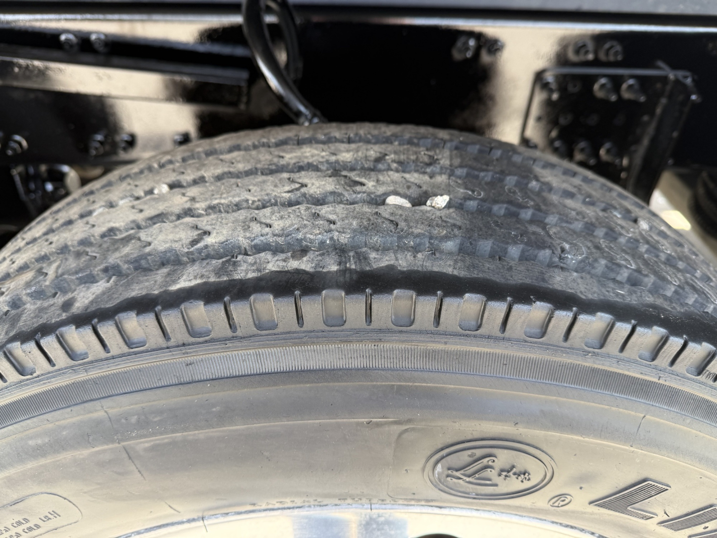 Truck wheel and tire in the engine/bay area showing tread details and wheel; no legible model text visible.