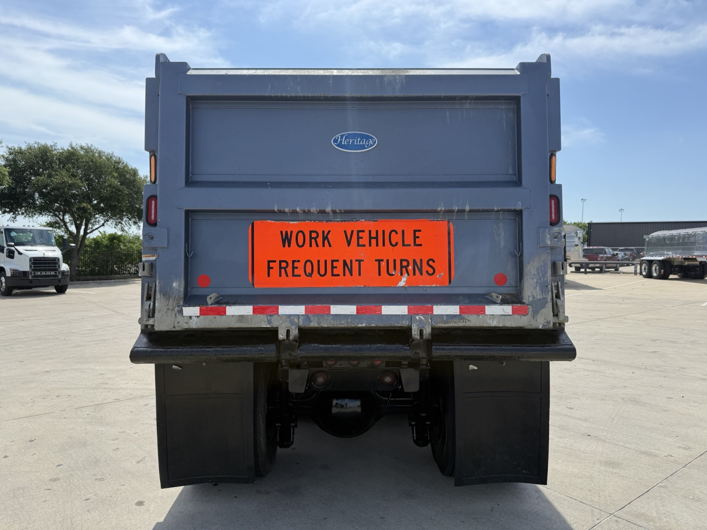 Volvo dump truck rear showing orange 'WORK VEHICLE FREQUENT TURNS' sign and rear bumper with mud flaps and hitch.