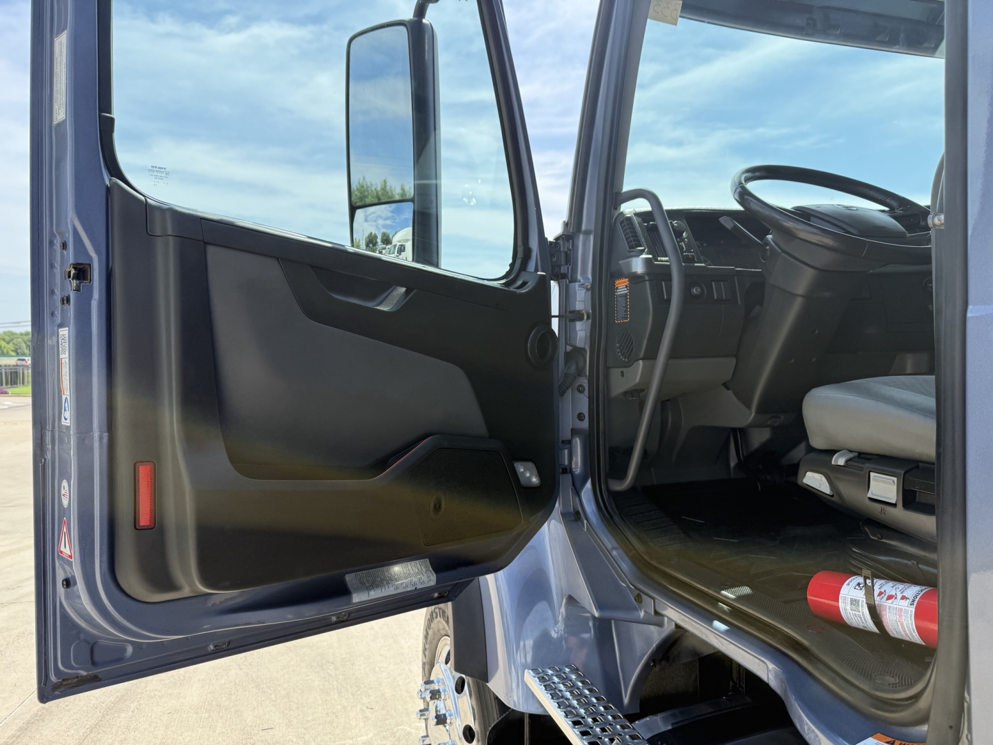 Cabin interior of a Volvo VHD truck with door open, showing steering wheel, driver's seat, and entry step.