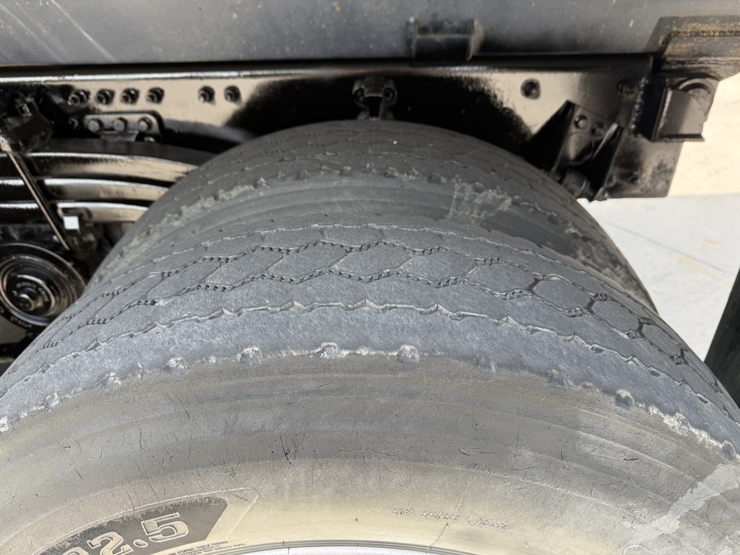 Truck rear wheel and suspension area with large dual tires, showing tread wear and undercarriage components.