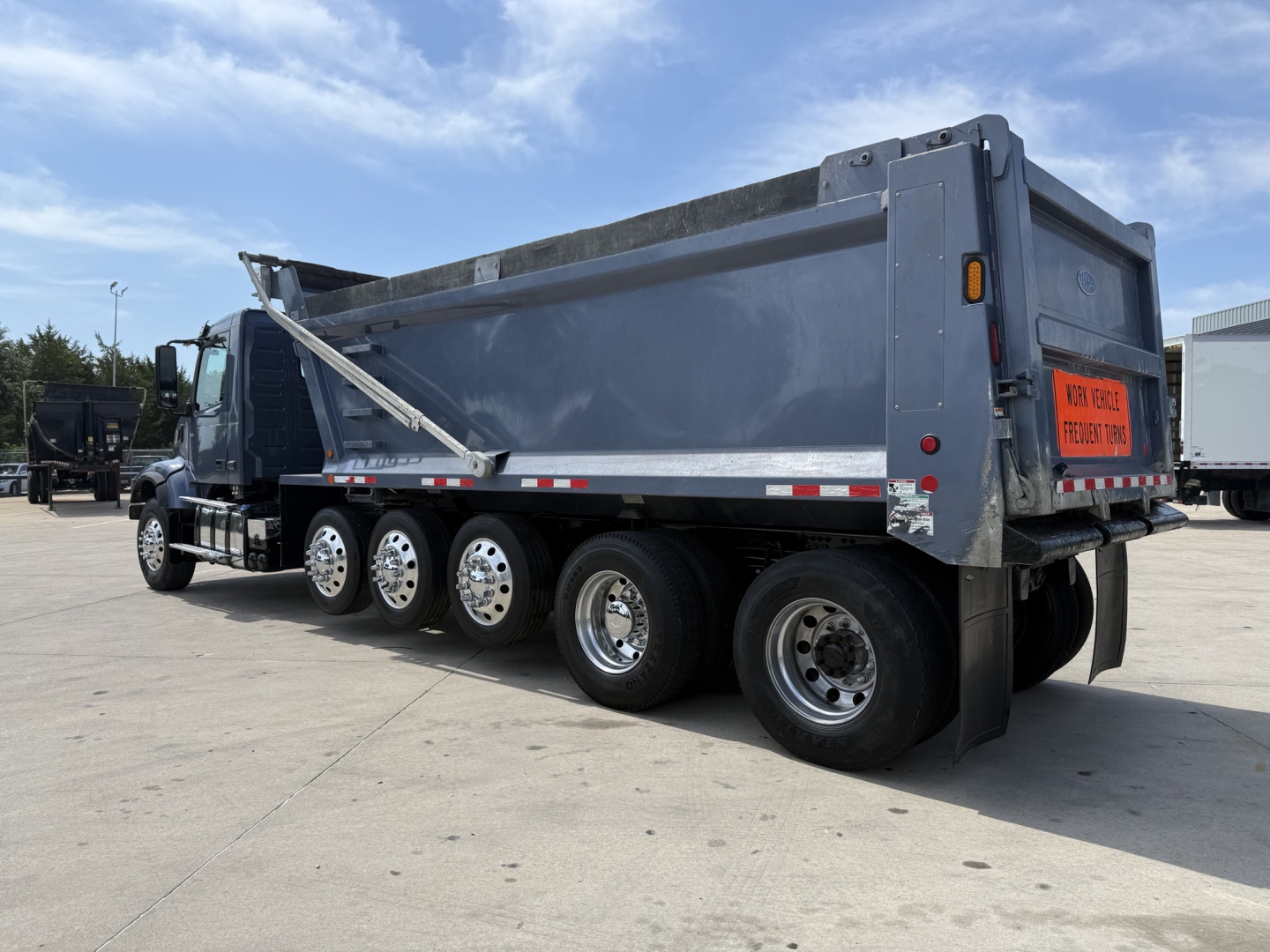 Volvo VHD dump truck side and rear showing multiple rear axles, dump bed, and orange warning sign on tailgate.