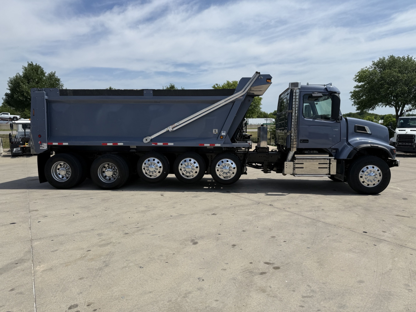 Dump truck side view showing cargo bed and multiple rear axles on a blue Volvo VHD truck.