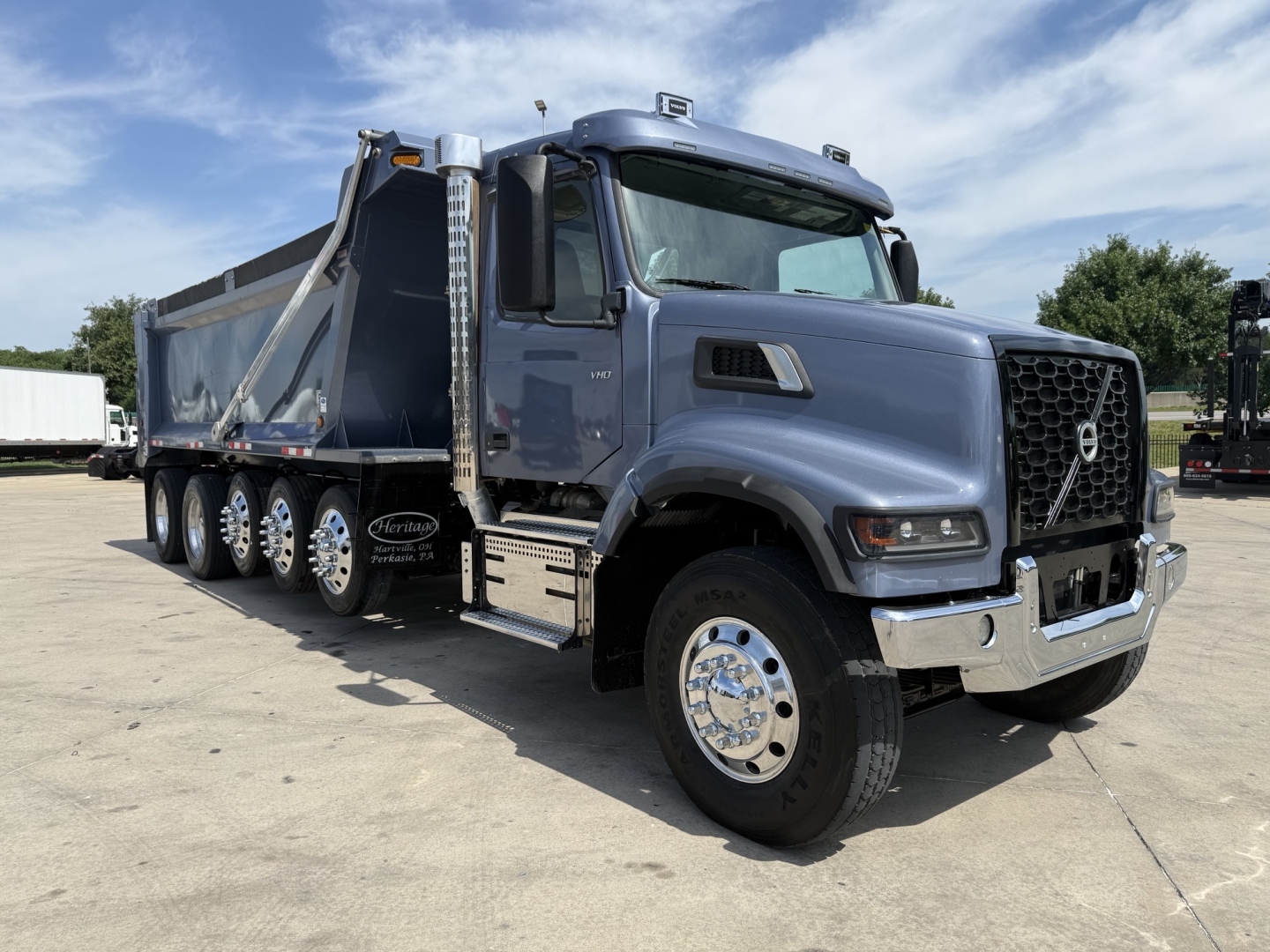 Volvo VHD dump truck in-service showing side and front view with blue-gray cab, large chrome bumper, multiple rear axles, and dump bed.