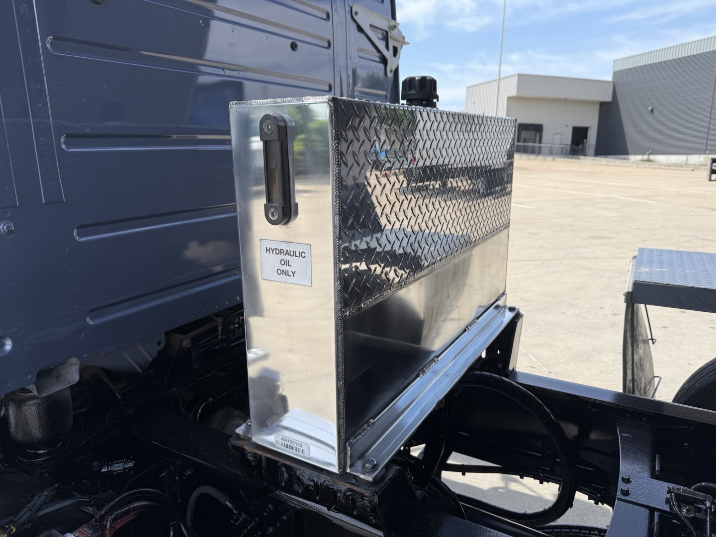 Truck VIN 4V5KJ9EH3RN652474 used dump truck with diamond plate tool/storage box mounted on side, hydraulic oil label, visible wheel and chassis components.