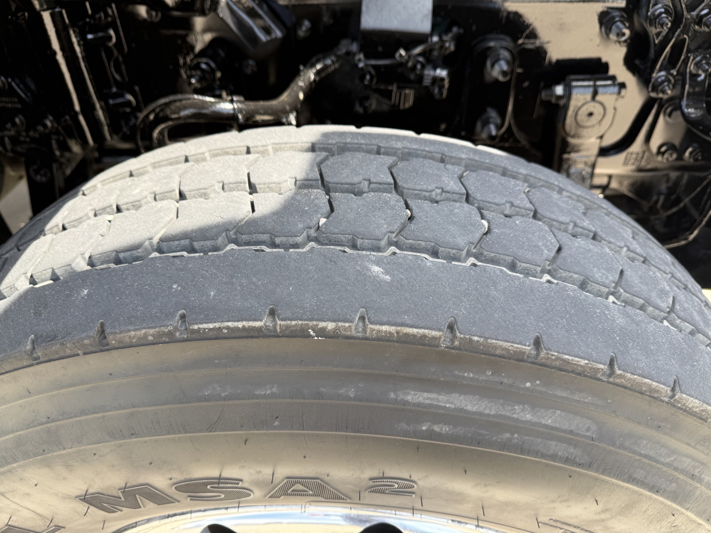 Truck drivetrain area and front tire of a Volvo VHD104F300 dump truck showing tire tread and partial engine bay components.