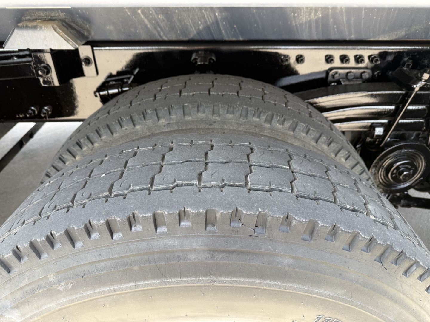 Truck rear suspension and large dual tires with tread pattern visible; chassis and leaf springs in view under a Volvo dump truck.