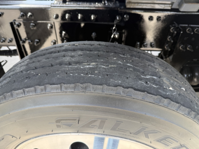 Tire and undercarriage of a Volvo dump truck showing a worn rear tire and chassis components.
