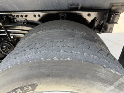 Truck rear wheel and suspension area with large dual tires, showing tread wear and undercarriage components.