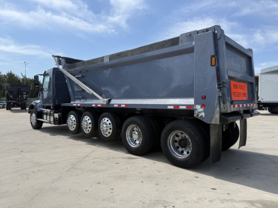 Volvo VHD dump truck side and rear showing multiple rear axles, dump bed, and orange warning sign on tailgate.