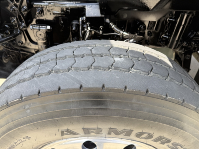 Truck wheel and front suspension area with tire tread and 'ARMOR' branding visible on the tire; engine bay components in background.