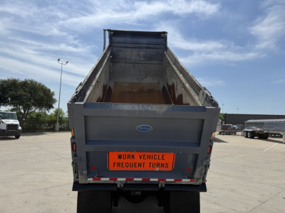 Dump truck bed of a Volvo work vehicle showing a bright orange warning sign with text 'WORK VEHICLE FREQUENT TURNS' on the tailgate.