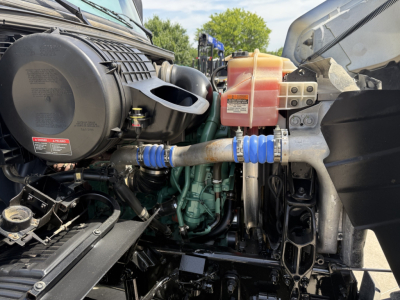 Volvo VHD powertrain area showing engine, radiator reservoir, hoses, and blue silicone hose with clamp in engine bay.