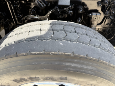 Truck drivetrain area and front tire of a Volvo VHD104F300 dump truck showing tire tread and partial engine bay components.