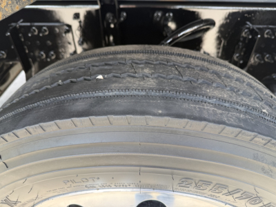 Truck wheel and frame showing tire with visible sidewall text. The tire reads PILOTA and 255/70, with wheel well and frame components surrounding.
