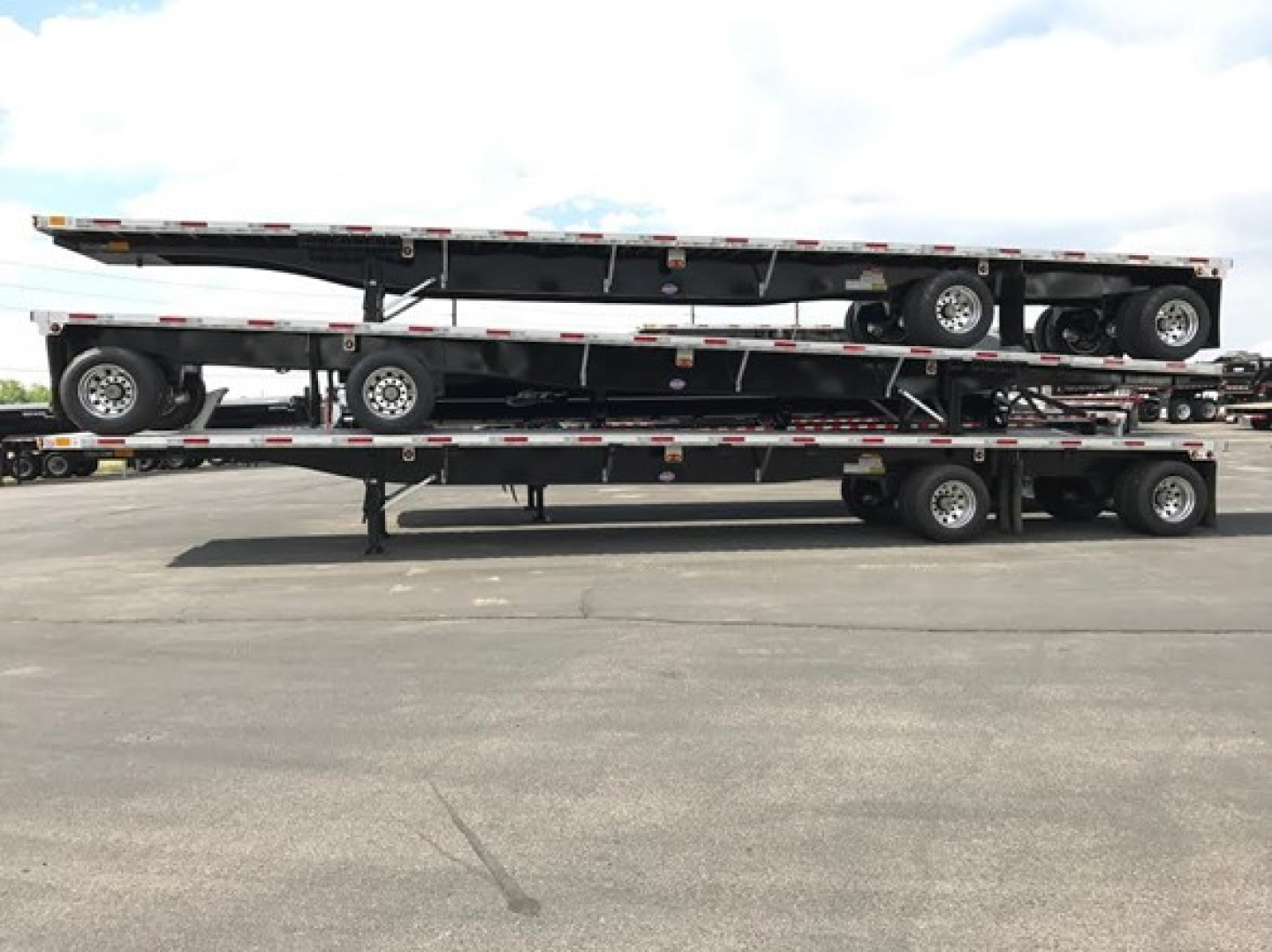 Flatbed trailer stack showing multiple levels of a Utility 4000Ae combo; two trailers on a lowboy with wheels and reflective safety rails.