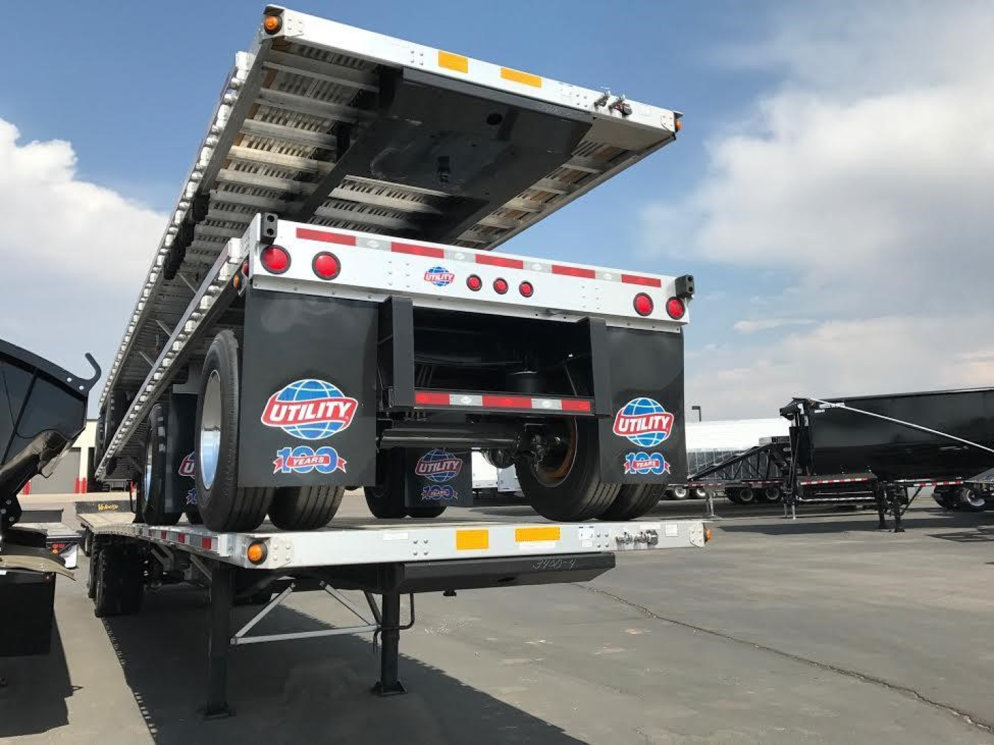 Utility trailer with flatbed ramp raised showing rear with Utility brand stickers and tandem wheels.