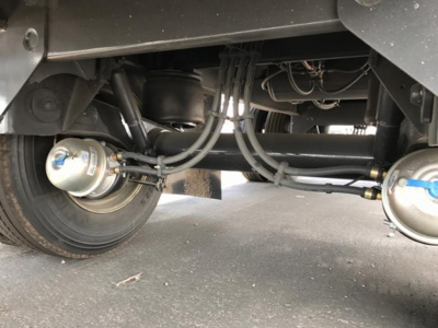 Axle undercarriage of trailer showing air brake hoses, cylinders, and suspension components.