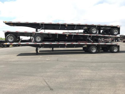 Flatbed trailer stack showing multiple levels of a Utility 4000Ae combo; two trailers on a lowboy with wheels and reflective safety rails.