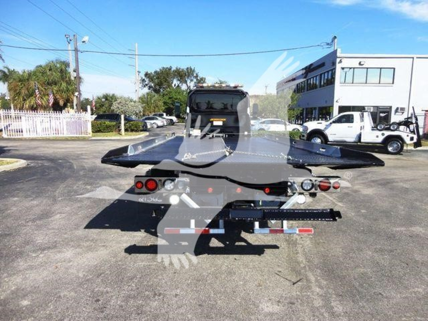 Towable rollback trailer with rear view showing dual red tail lights and license plate area, back of trailer, equipment in a parking lot.