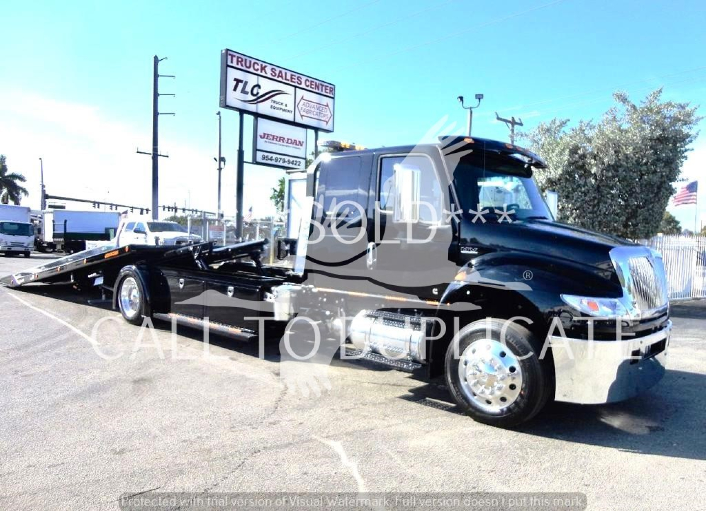 International MV rollback truck in black with a long chrome bumper and wheel-well chrome; visible text on truck windows and signs in background.