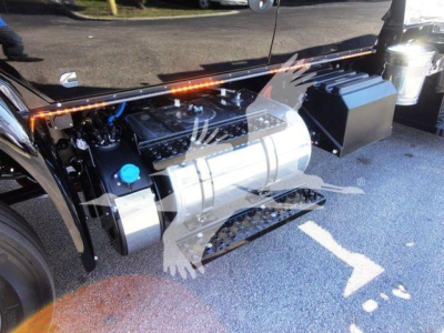 Truck engine bay with large cylindrical silver fuel tank and black components; visible label text not legible