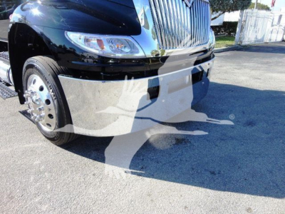International MV truck front bumper and grille with chrome wheels visible in a rollback dealership lot.
