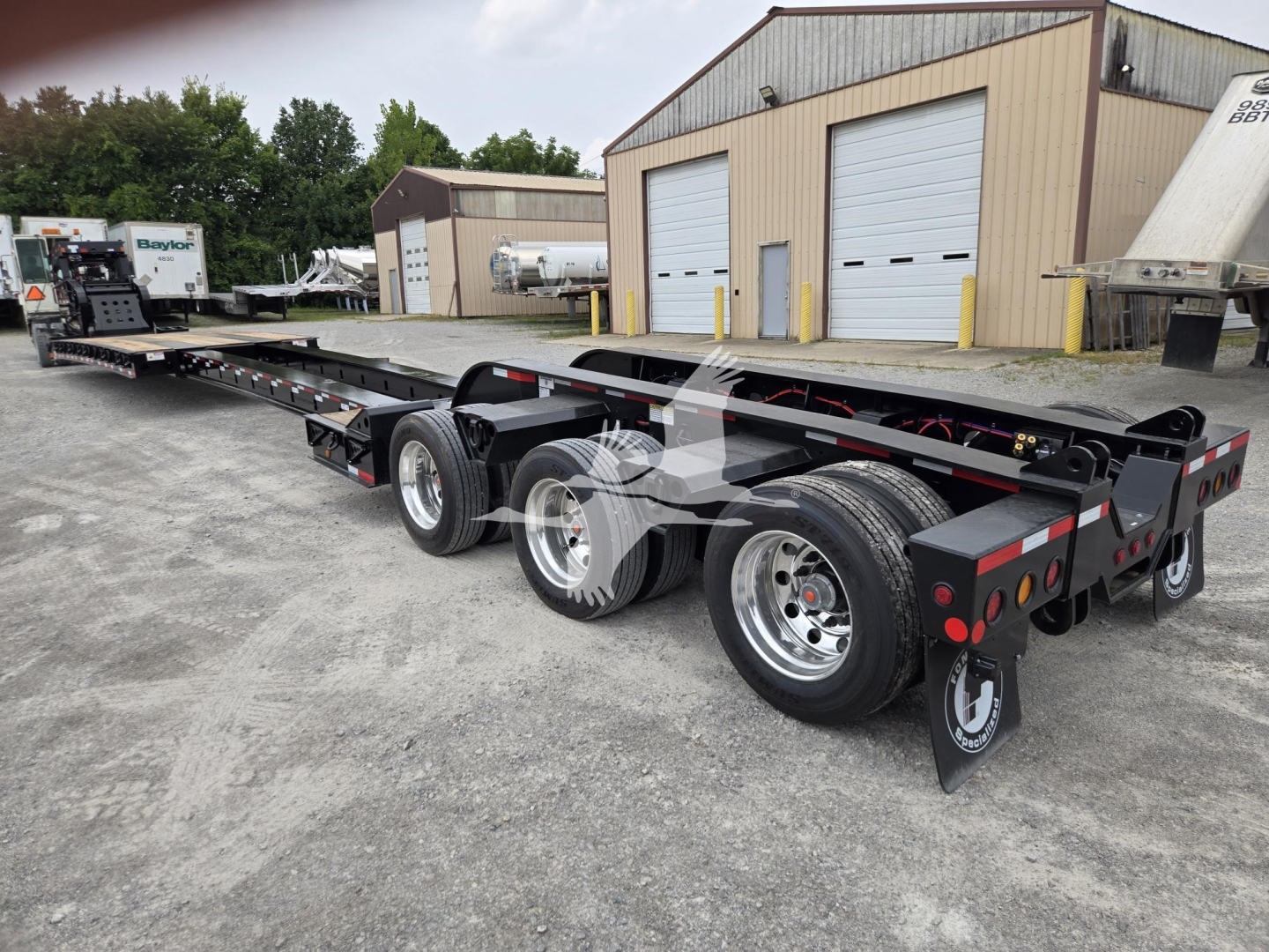 Lowboy trailer showing Fontaine 60Hd MX with long flatbed and dual rear axles, black frame, chrome wheels, side rails, and rear safety features.
