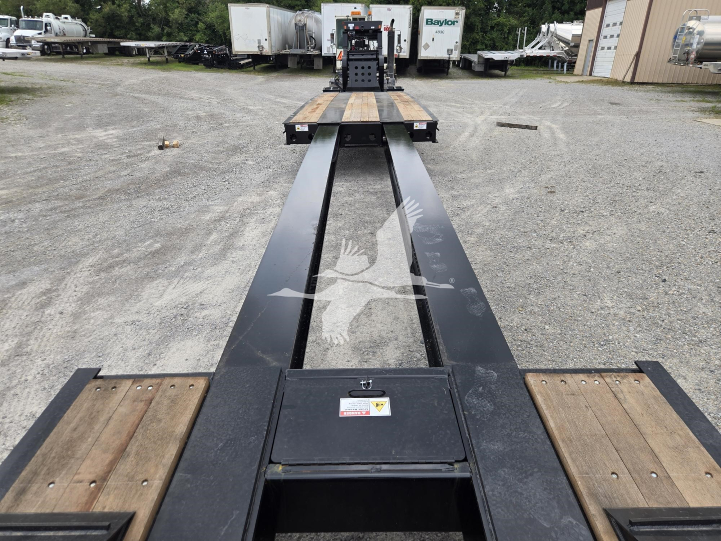 Lowboy trailer deck with long black I-beam frame and wooden deck sections; Fontaine 60Hd MX trailer in distance; VIN 13NE58306V35A7290 stock V35A7290.