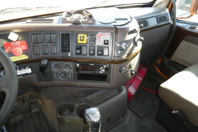 Cab interior of a 2012 Volvo VNM42T truck showing dashboard with multiple dials, radio, climate controls, gear shifter, and steering wheel.