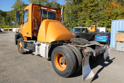 Volvo VNM42T daycab tractor showing front wheel, cab, and sleeper with bright orange chassis and attached snow plow/waste shield.
