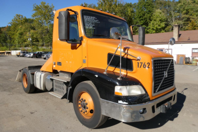 Volvo VNM42T conventional daycab truck in orange and black with number 1762 on door, front grille, side mirrors, and dual fuel tanks visible.
