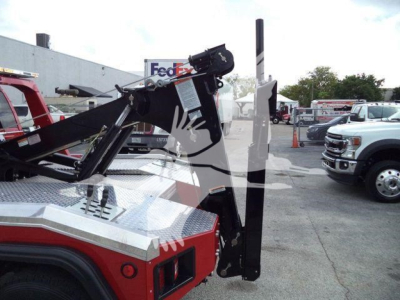 Tow truck with winch assembly and hydraulic boom showing controls and metallic deck, FedEx truck in background.